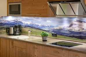 Una cucina con uno schienale decorato con un paesaggio montano, una macchina da caffè, un lavandino e una piccola pianta in vaso.