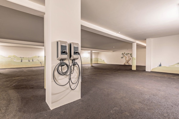 Un espace de stationnement intérieur doté de deux bornes de recharge pour véhicules électriques, d’un sol en béton et d’une fresque murale.