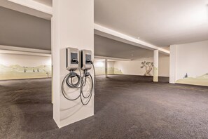Sisätilojen pysäköintialue, jossa on kaksi sähköautojen latauspistettä, betonilattia ja seinällä suuri seinämaalaus.