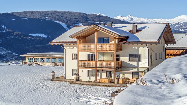 Ein mehrstöckiges Chalet mit Balkon vor einer verschneiten Berglandschaft.