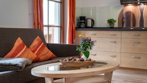 Ein modernes Wohnzimmer mit einer Couch, einem Couchtisch mit einer Nussmischung und einer Küchenzeile mit Schränken und einer Kaffeemaschine.