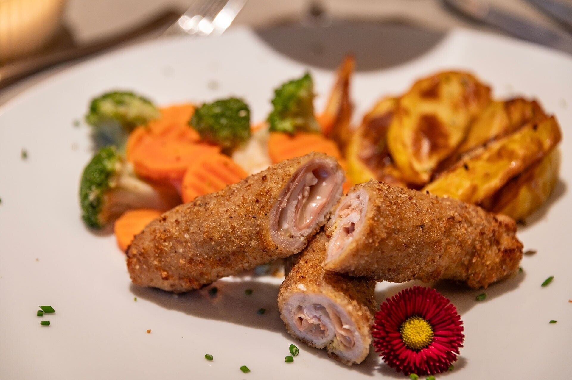 Une assiette contenant un plat pané et frit, peut-être du poulet, accompagné de légumes et d'une petite décoration florale.