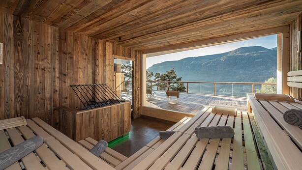Une cabane en bois dotée d’un sauna, d’une terrasse en bois et offrant une vue sur les montagnes et l’eau.