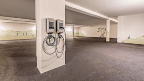 Ein überdachter Parkbereich mit zwei Ladestationen für Elektrofahrzeuge, einem Betonboden und einem Wandgemälde.