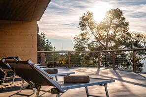 Une terrasse sur le toit, équipée de chaises longues, d’une table et offrant une vue sur les arbres et une étendue d’eau.