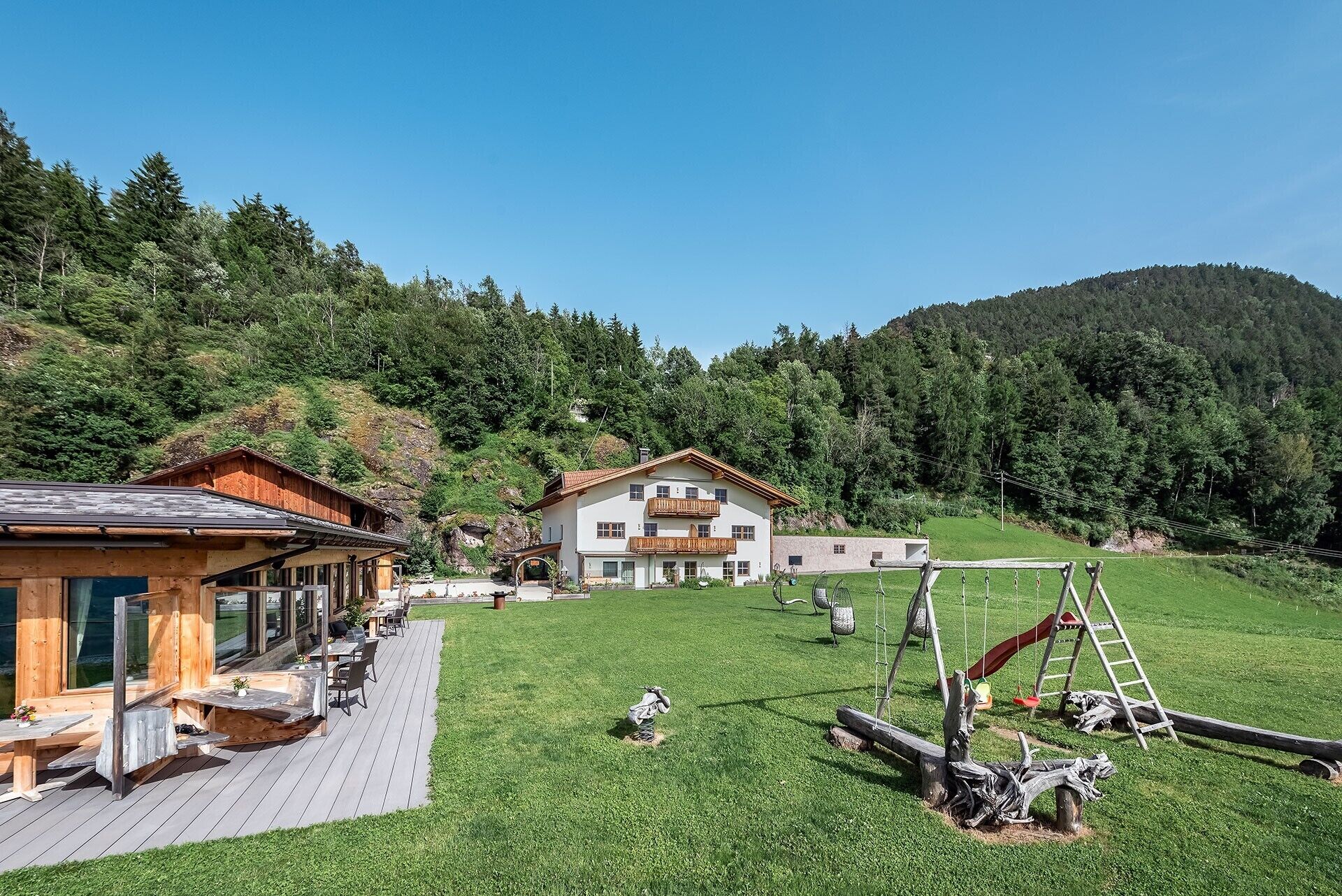 A chalet with a deck, a play area, and a mountain backdrop.
