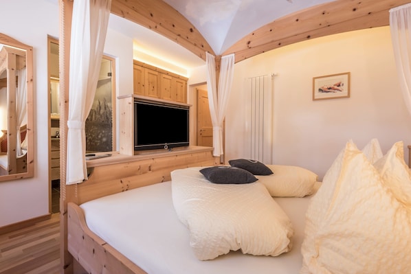 Une chambre à coucher avec un lit en bois, une télévision et une fenêtre avec des rideaux.