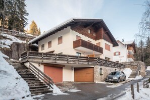 A multi-story building with a wooden balcony, a staircase leading to the entrance, and a parked car.