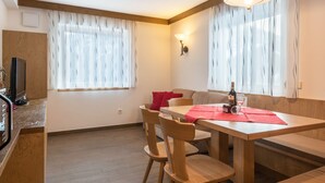 A dining area with a wooden table, chairs, a bench, and a wine bottle. - Cosy Apartment “Ulrica” with Mountain View, Wi-Fi, Balcony & Terrace (St. Ulrich / Gröden)
