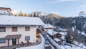 A snow-covered mountain village with chalet-style buildings, a paved driveway, and a clear view of the surrounding mountains. - Cosy Apartment “Ulrica” with Mountain View, Wi-Fi, Balcony & Terrace (St. Ulrich / Gröden)