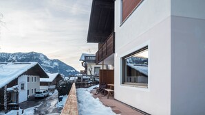 Een modern gebouw met een balkon en uitzicht op een besneeuwde berg, met een geparkeerde auto.