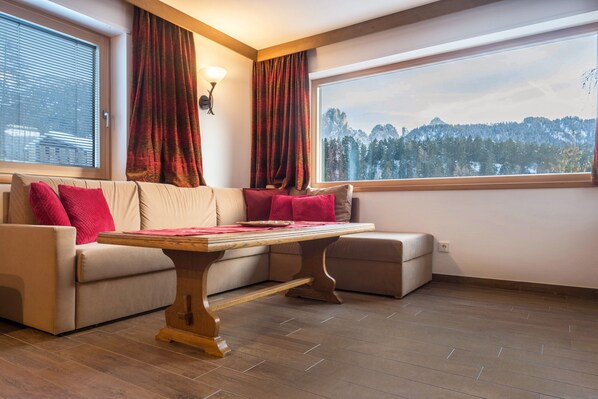 A room with a sofa, a table, and a view of a mountainous landscape.