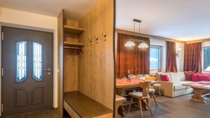 Een kamer met een houten deur, een bankje, een eettafel met stoelen, een bank en een raam met gordijnen.