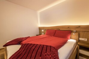 A neatly made bed with a red blanket and pillows, a wooden headboard, and a bedside table with a lamp.