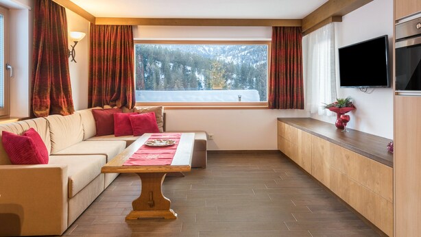Een moderne woonkamer met een bank, een houten salontafel, een televisie en een keuken met uitzicht uit het raam.