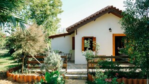 A small, single-story house with a tiled roof and a porch. There is a garden with various plants and flowers in front of the house.