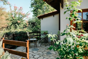 A patio with a stone floor, a wooden bench, and a table with chairs.