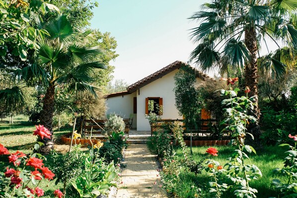 A rustic house with a tiled roof, surrounded by lush greenery and flowering plants.