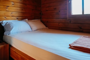 A wooden cabin room with a bed, pillows, and a window.
