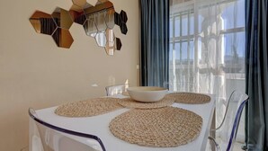 A dining area with a white table, clear chairs, and a decorative hexagonal mirror on the wall.