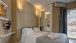 A hotel room with a bed, a mirror, a window with curtains, and a wall-mounted air conditioner.
