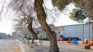 A playground with swings and a slide, benches, and a large tree in the center. - Zita - Spacious Apt with 2 Bedrooms & 2 Bathrooms, Kaštel Novi (Kaštel Novi)