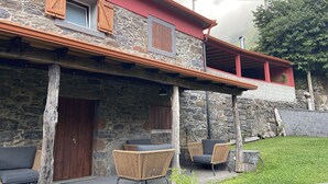 A stone building with a wooden door, two wicker chairs, and a red balcony. - House in the Mountains With Garden (São Vicente)