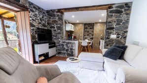 A cozy living area with a stone wall, a sofa, a coffee table, and a TV. - House in the Mountains With Garden (São Vicente)