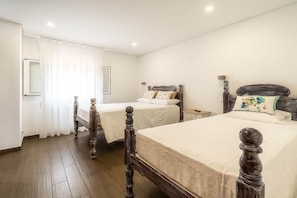 Un dormitorio con dos camas individuales, cabeceros de madera, ropa de cama blanca y una mesita de noche pequeña con una lámpara.