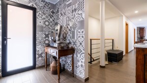 A modern interior with patterned tiles, a wooden desk, a black ottoman, and a staircase. - House in the Mountains With Garden (São Vicente)