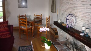 A dining area with a round wooden table, four wooden chairs, a vase with a pink flower, a brick wall, and a fireplace.