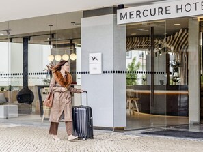 Ein Hotel Eingang mit einem Schild, auf dem 'MERCURE HOTEL' steht, einer Glastür und einer Person mit einem Koffer.