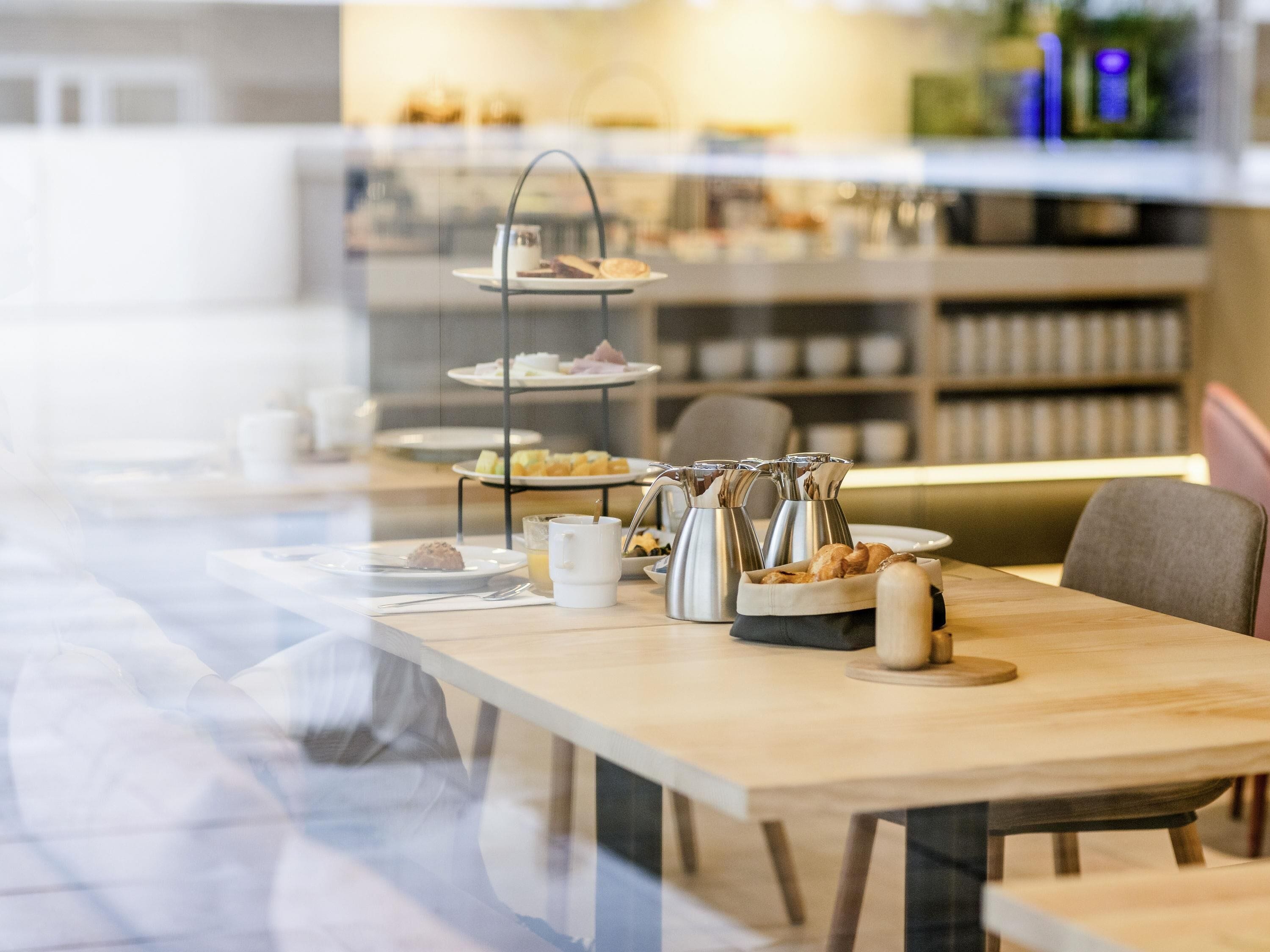 A breakfast buffet setup with tiered serving dishes, a coffee pot, and a fruit bowl on a wooden table.
