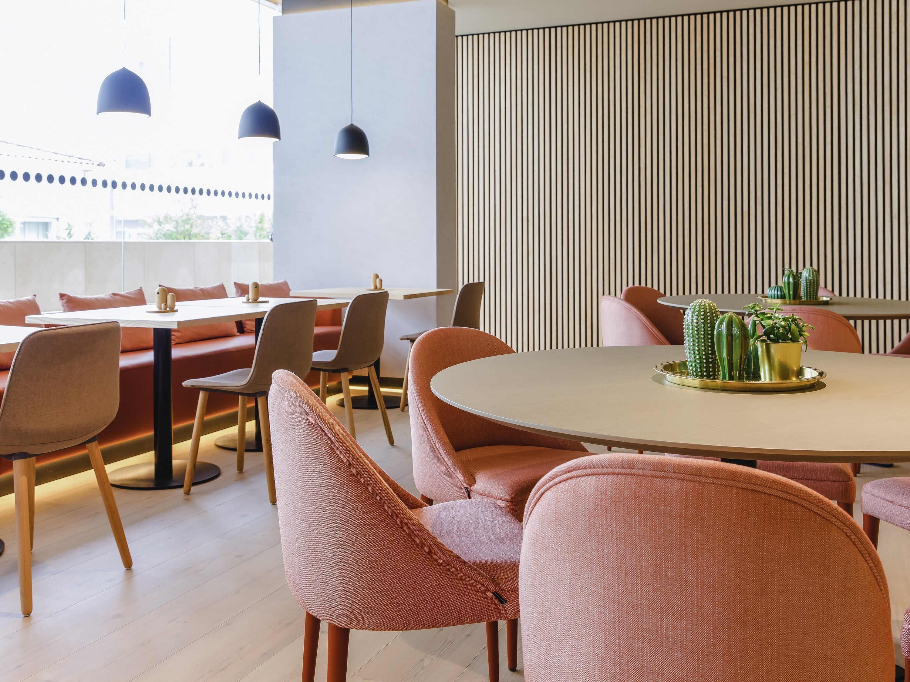 A modern dining area with round tables, cushioned seating, pendant lighting, and a vertical striped wall.