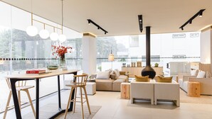 Una sala de estar moderna con comedor, ventanas amplias y una cocina al fondo.
