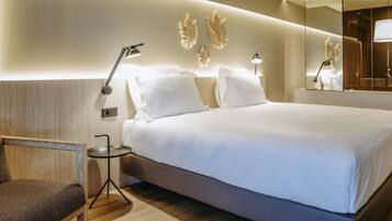 Quarto de hotel moderno com uma cama grande, luminárias laterais, uma cadeira e um espelho.