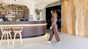 Un área de recepción moderna con un mostrador curvo, taburetes de bar y una pared de madera con un diseño único.