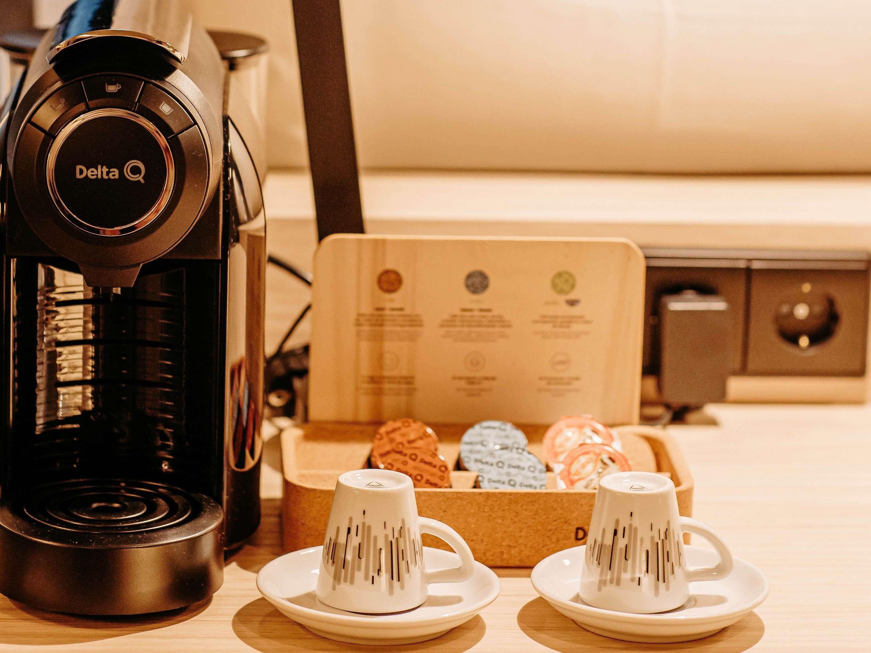 Une machine à café, deux tasses et une boîte de pâtisseries sur une table.