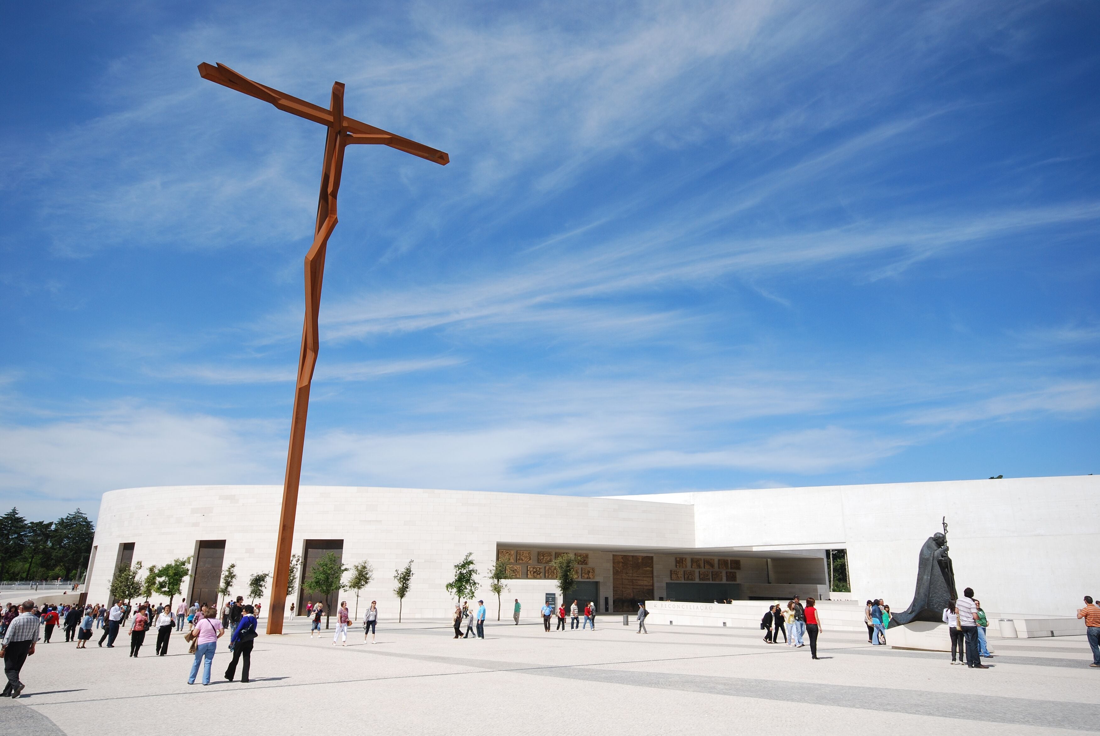Un edificio moderno con una gran cruz de madera y una escultura de una figura.