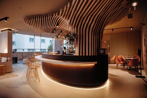 Uma área de recepção moderna com balcão curvo, ripas de madeira no teto e um espaço de estar com cadeiras e uma mesa.