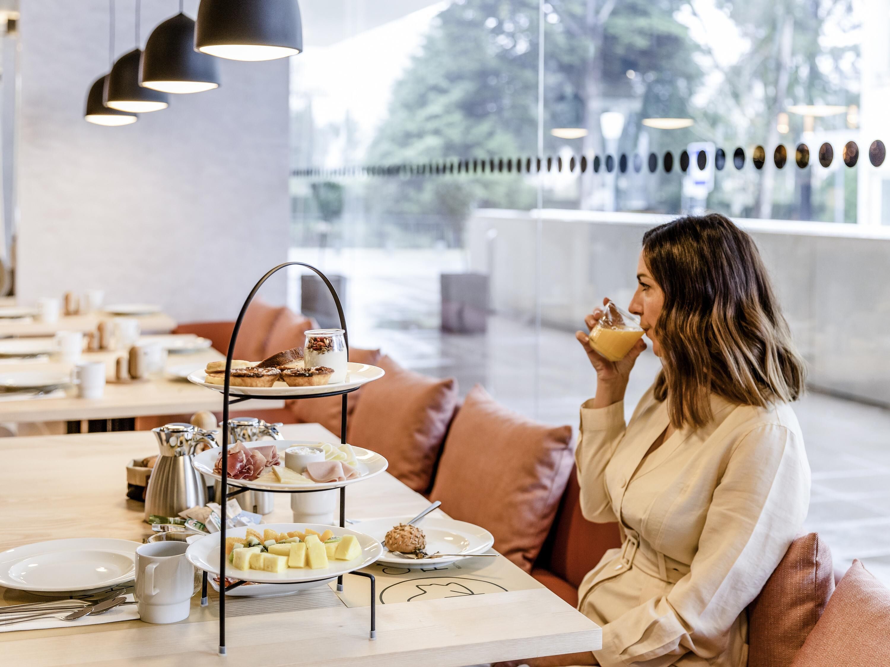 Una donna seduta a un tavolo con un vassoio a più piani per dolci, piatti di cibo e una caffettiera.