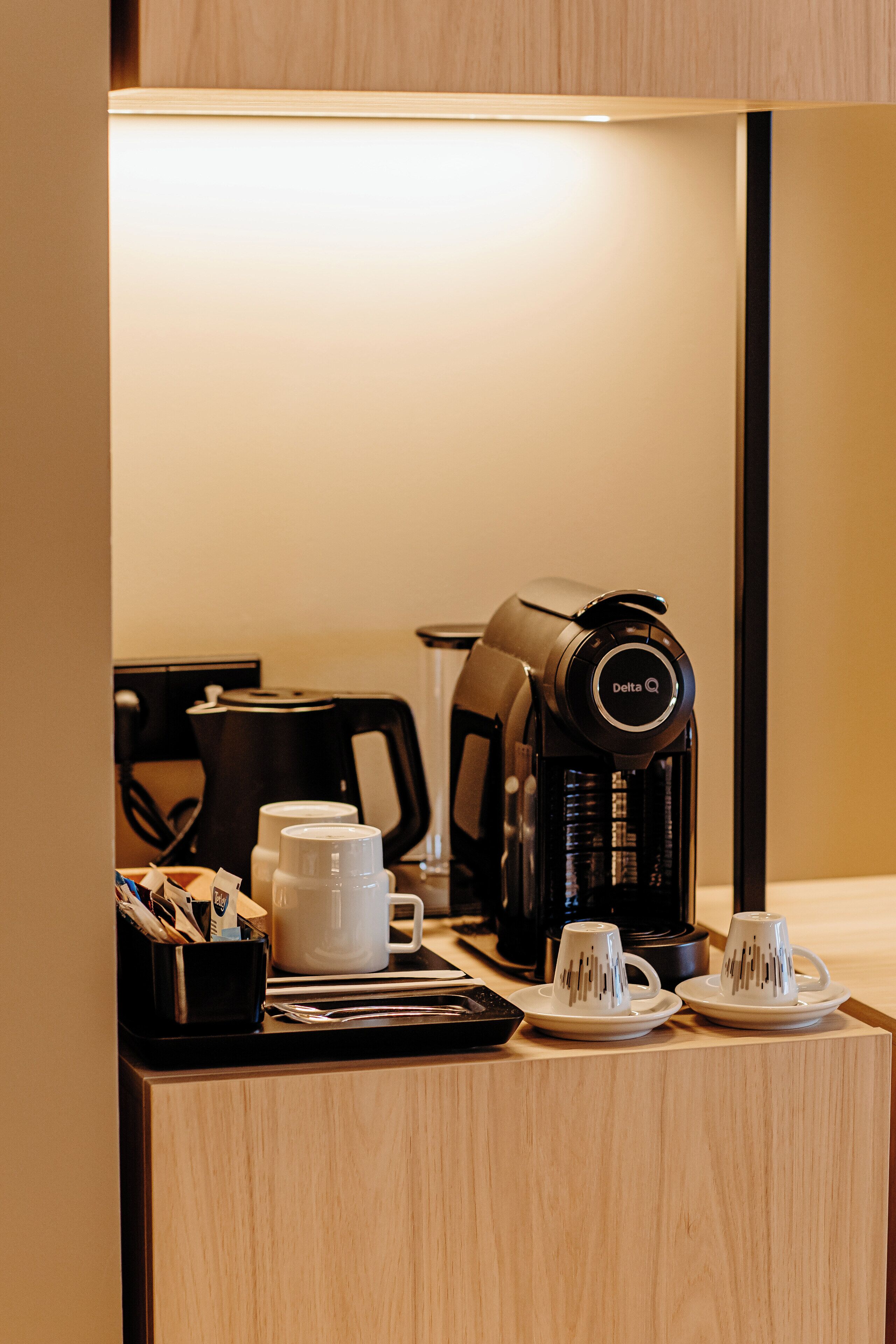 A hotel room's coffee station with a coffee maker, cups, and a tray.