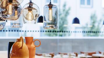 L’intérieur d’un restaurant, avec des luminaires suspendus, une table ornée d’un vase et d’une carafe, et une vue sur les bâtiments à l’extérieur.
