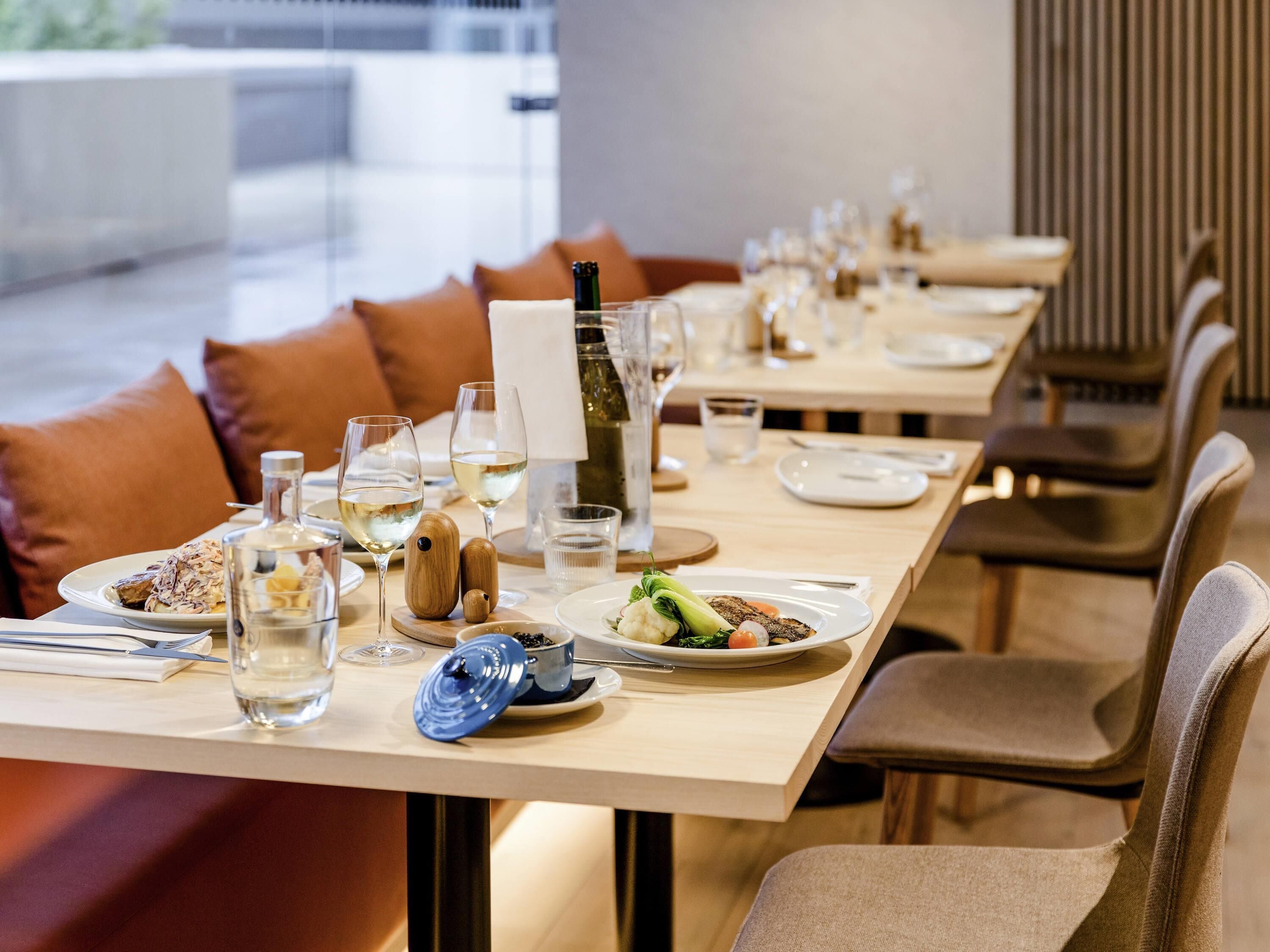 Comedor con mesas dispuestas para comidas, incluyendo platos, vasos y una botella de vino.