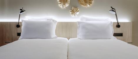 Un lit double avec du linge de lit blanc, deux tables de chevet avec des lampes et des feuilles décoratives fixées au mur.