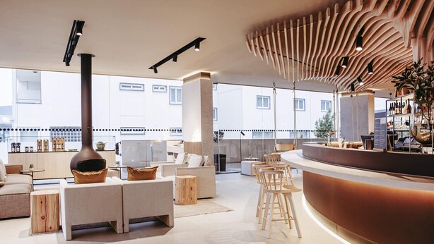 Zona de bar moderna con un mostrador curvo, taburetes de madera y un techo alto con luminarias únicas.