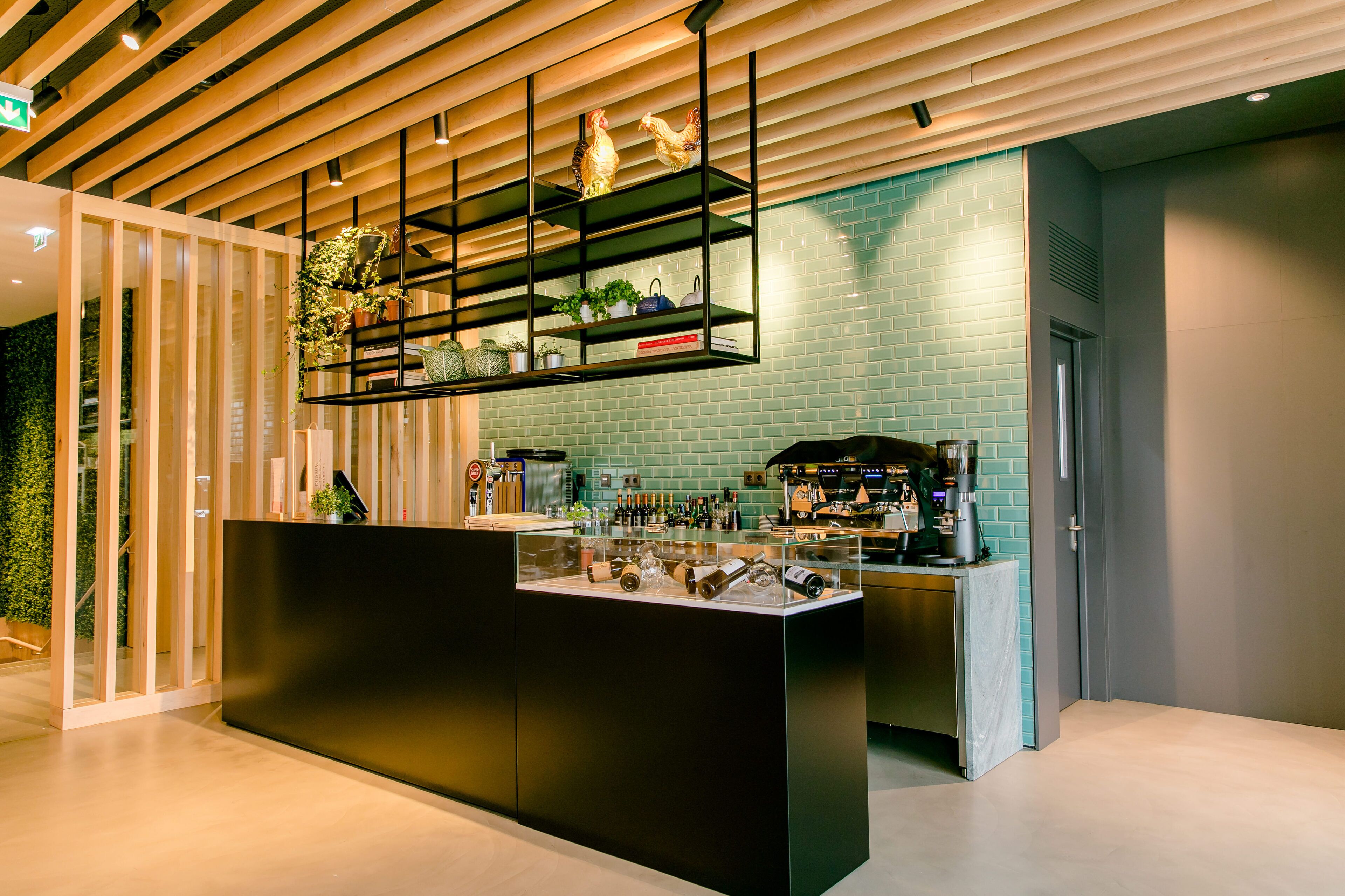A modern bar area with a black counter, shelves with plants, and a brick wall.