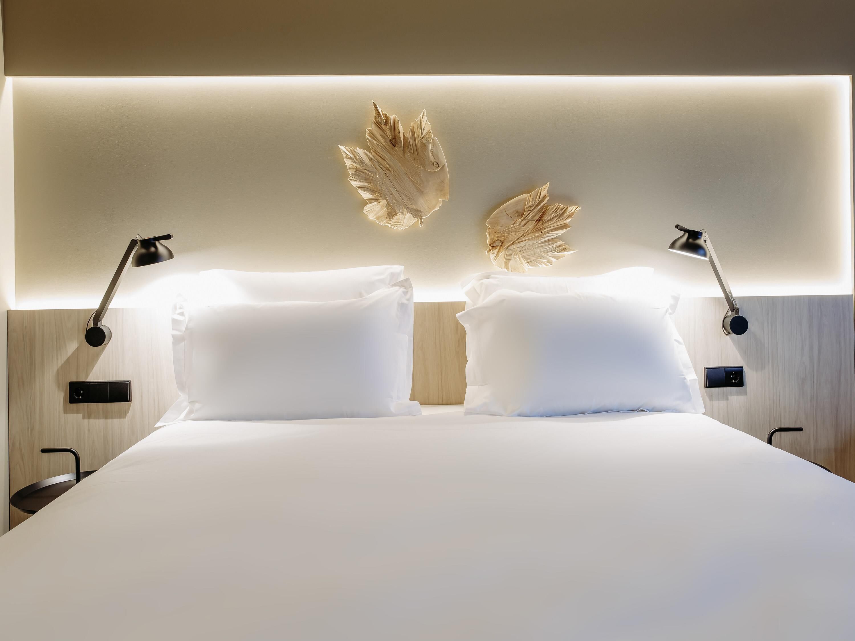 Una habitación de hotel moderna con una cama bien hecha, dos lámparas de noche y una decoración de pared ornamental.
