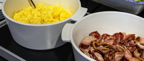 Three bowls of food on a stove: scrambled eggs, bacon, and a salad.