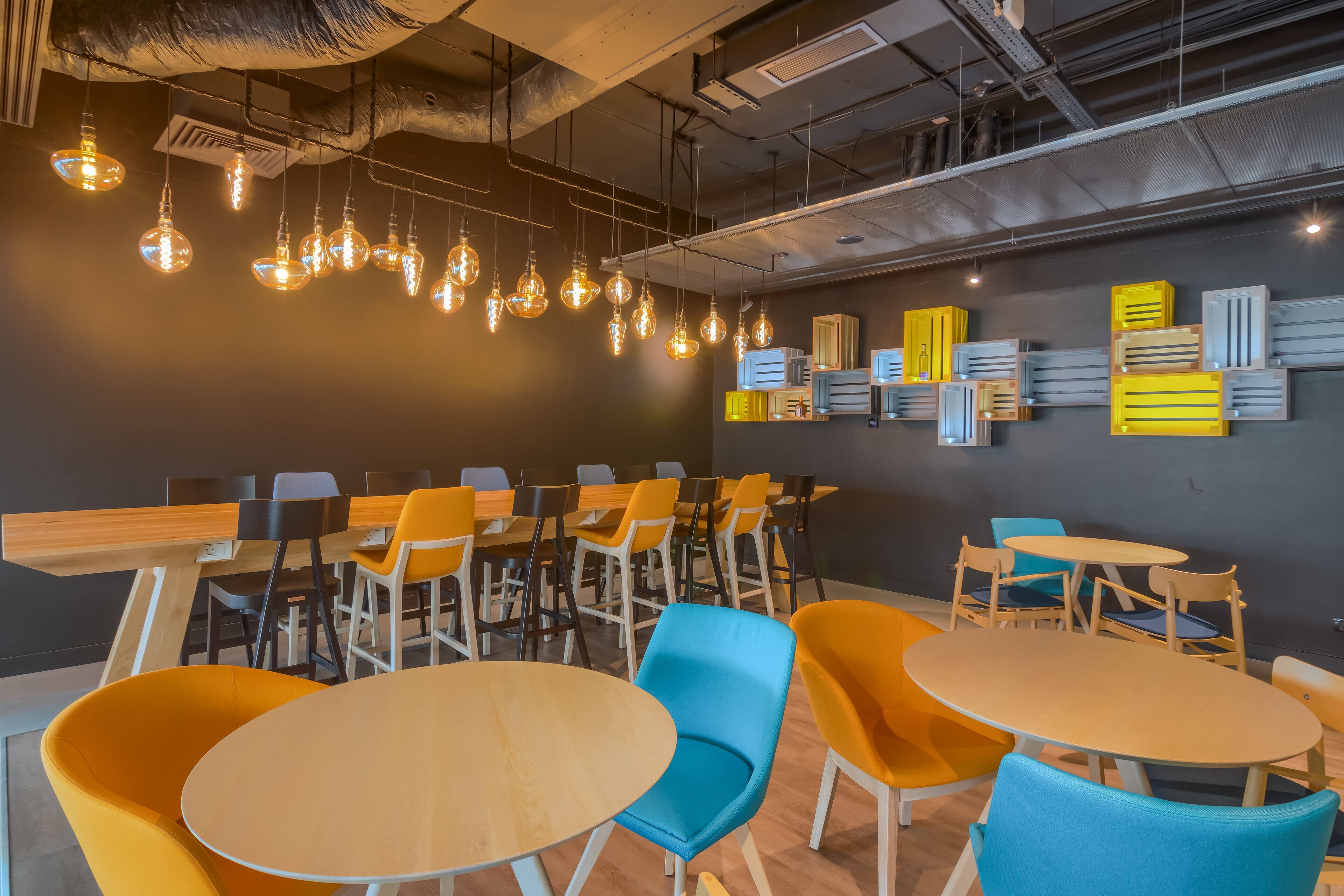 A modern conference room with round tables and colorful chairs, overhead lighting, and storage units on the wall.